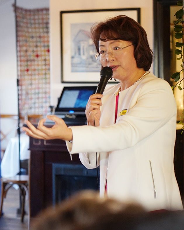 Soo Yoo in a white jacket speaking into a microphone