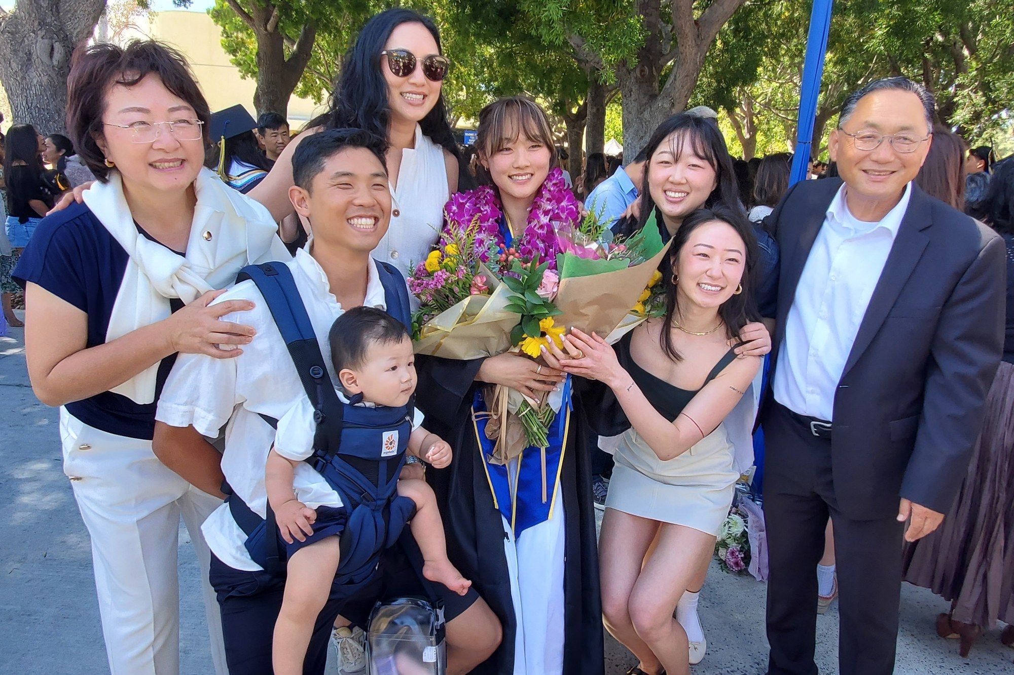 Soo Yoo and her family smiling together outdoors at a graduation, around a daughter in a cap and gown holding flowers
